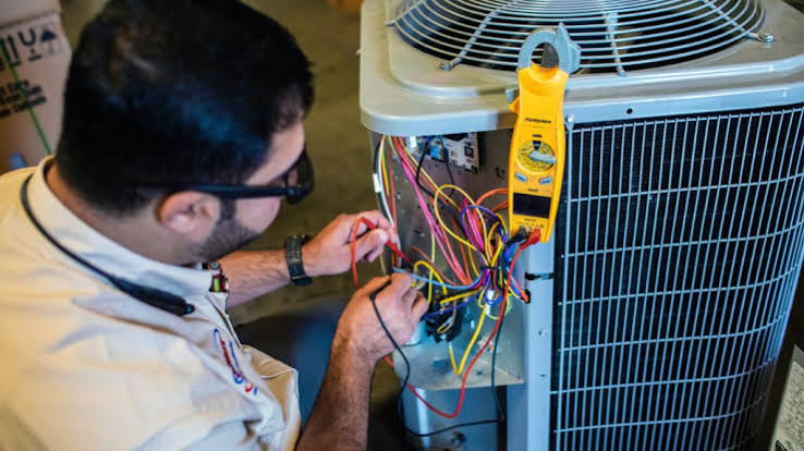 Technician using a clamp meter to diagnose wiring in an outdoor air conditioning unit