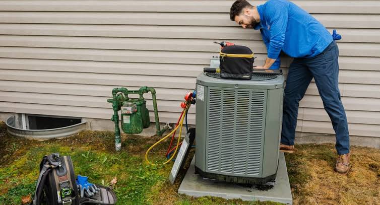 Technician checking an outdoor air conditioning condenser beside a house