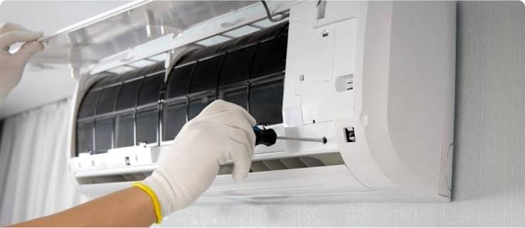 Gloved hands servicing the open filter area of a wall-mounted indoor air conditioner